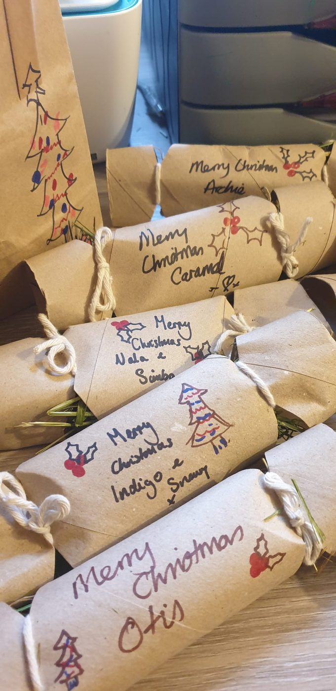 Hand drawn Christmas crackers filled with hay, each labelled with a guest's name